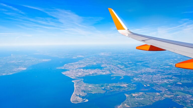 Top 8 Budget Airlines Compared: Which Offers the Best Value in 2026? View from airplane window showing wing over coastline and blue ocean.